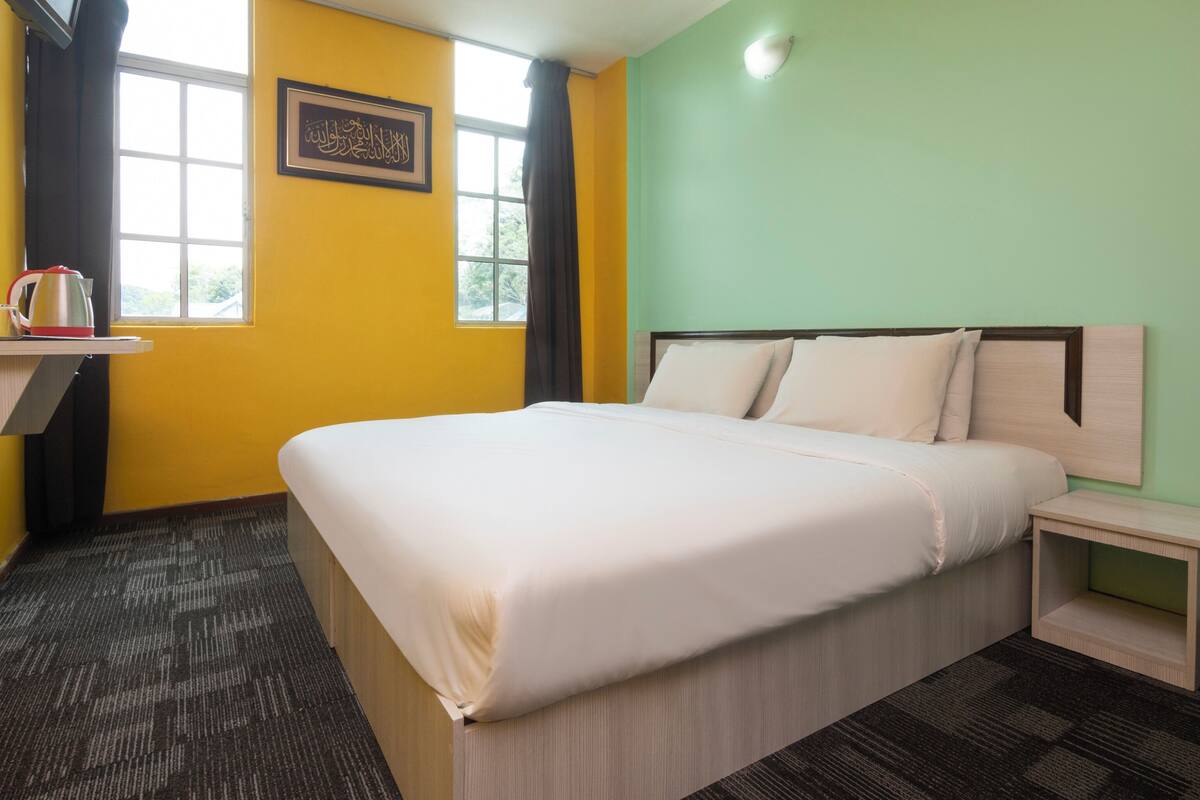 A hotel room with a bed, a bedside table, a window, a picture frame, and a curtain.