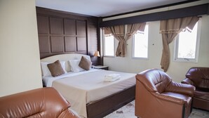 A bedroom with a large bed, two brown leather chairs, a nightstand, and a window with curtains.