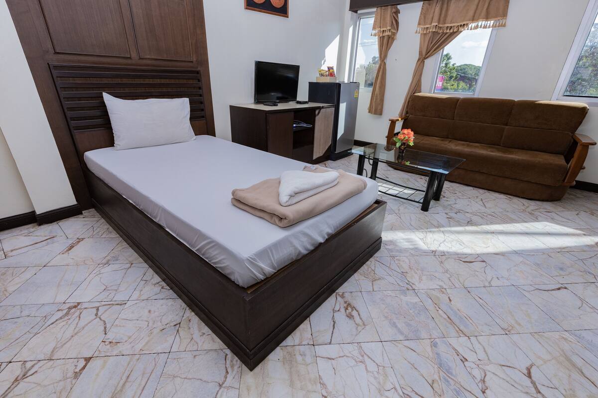 A hotel room with a large bed, a sofa, a TV, and a refrigerator.