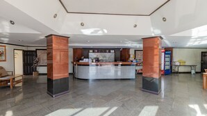 A reception area with a marble counter, two wooden pillars, and a tiled floor.