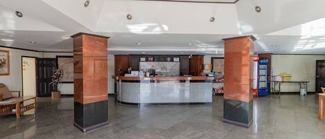 A reception area with a marble counter, two wooden pillars, and a tiled floor.