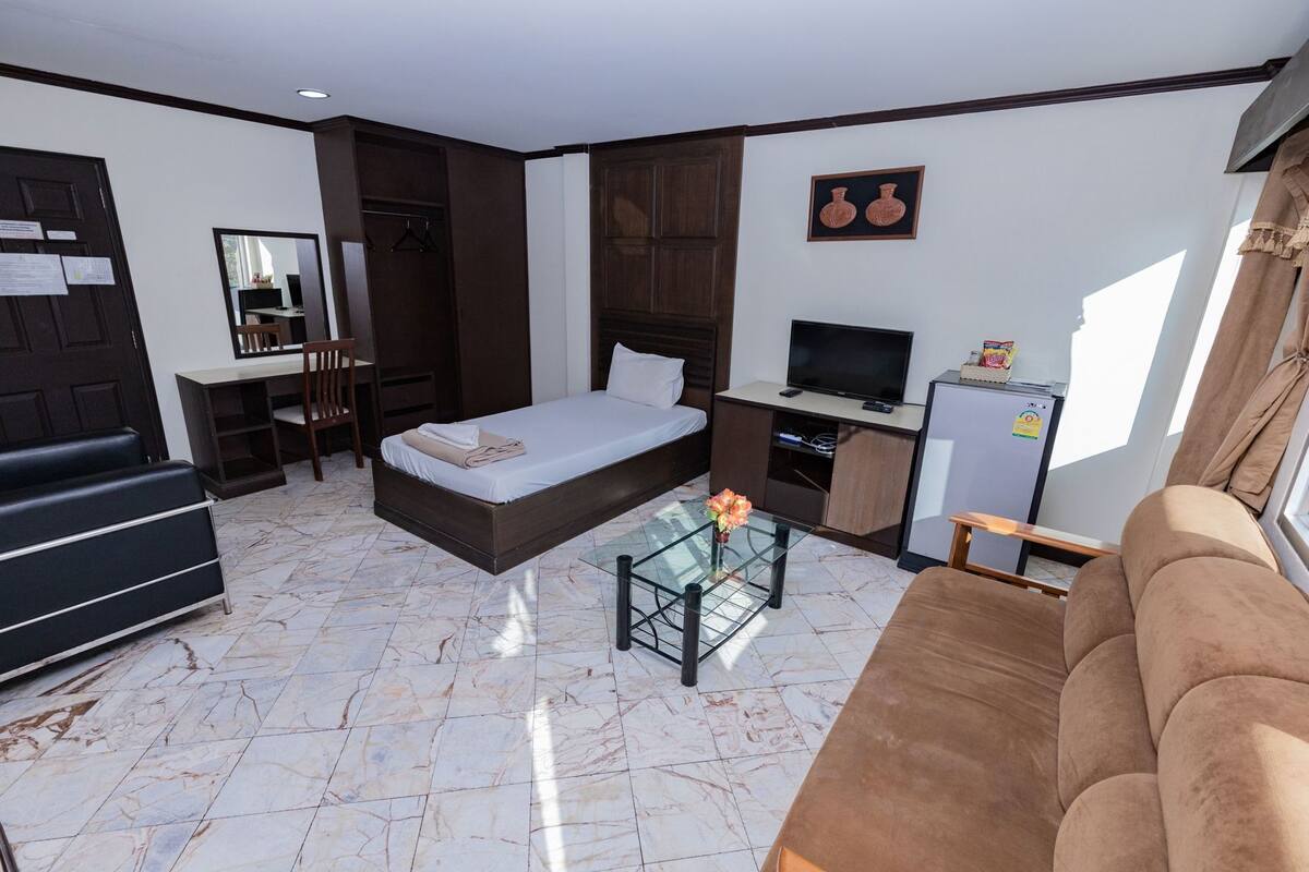 A compact hotel room with a bed, a sofa, a TV, a small table, and a mirror.