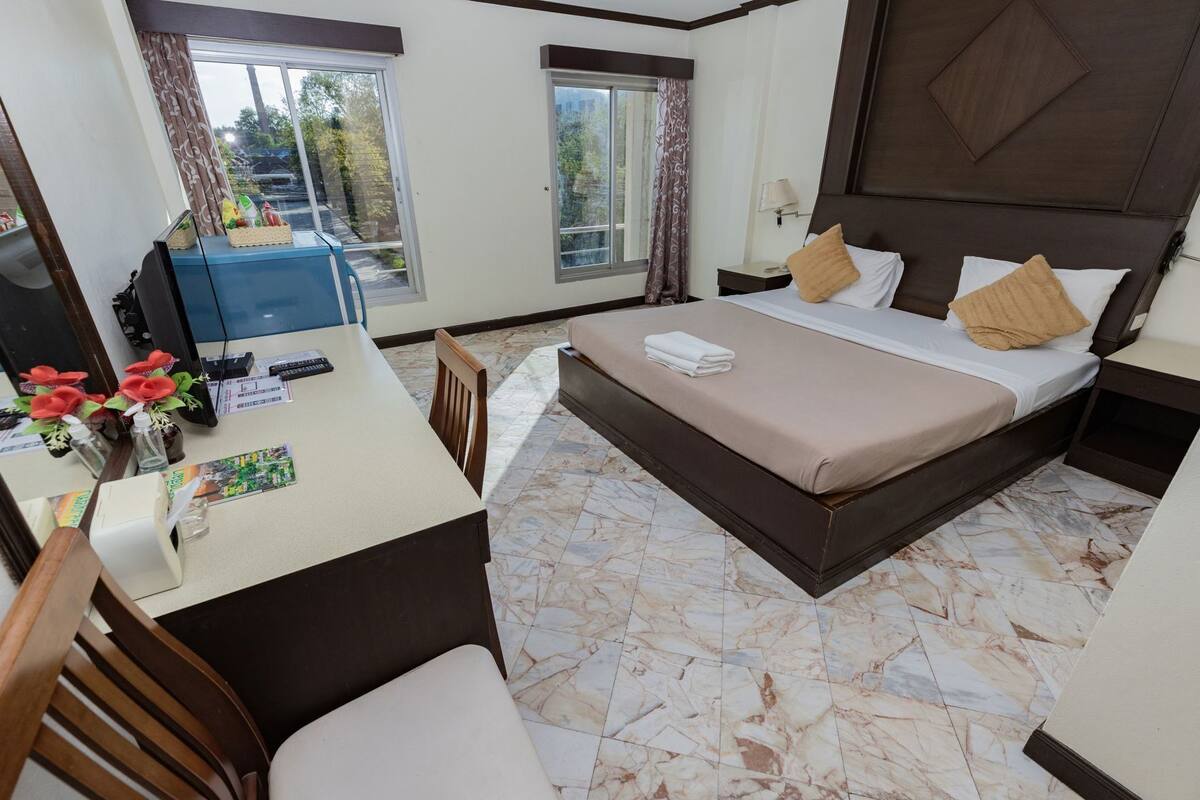 A hotel room with a bed, bedside table, desk, chair, and a view through the window.