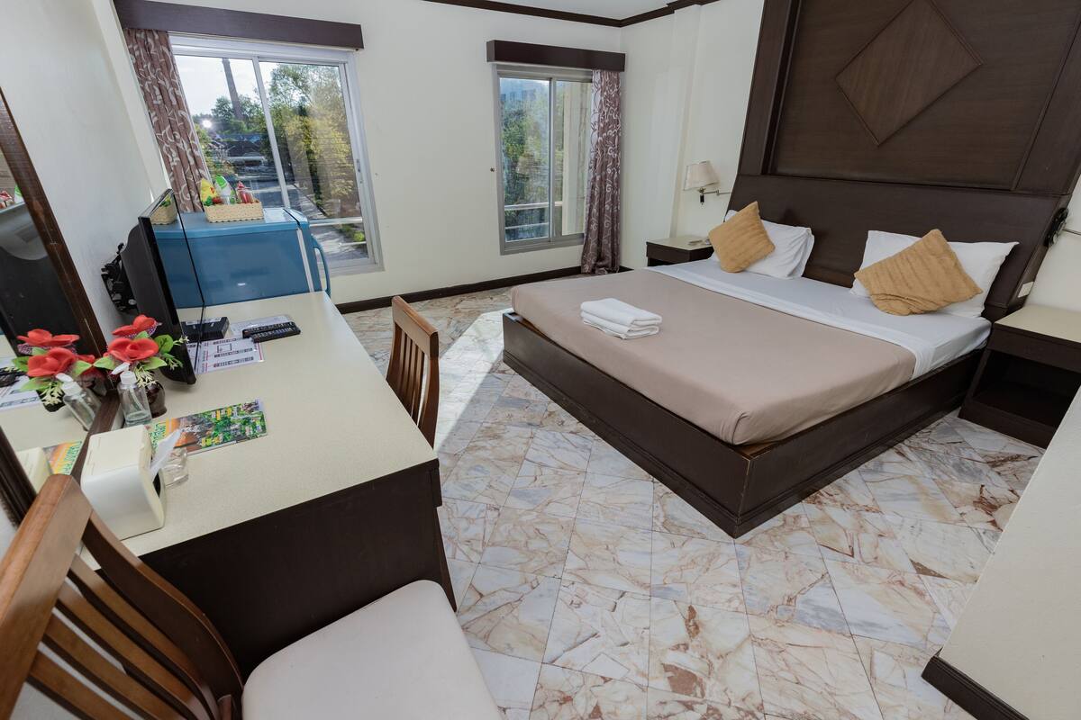 A hotel room with a bed, a desk with a chair, a television, and a window with curtains.