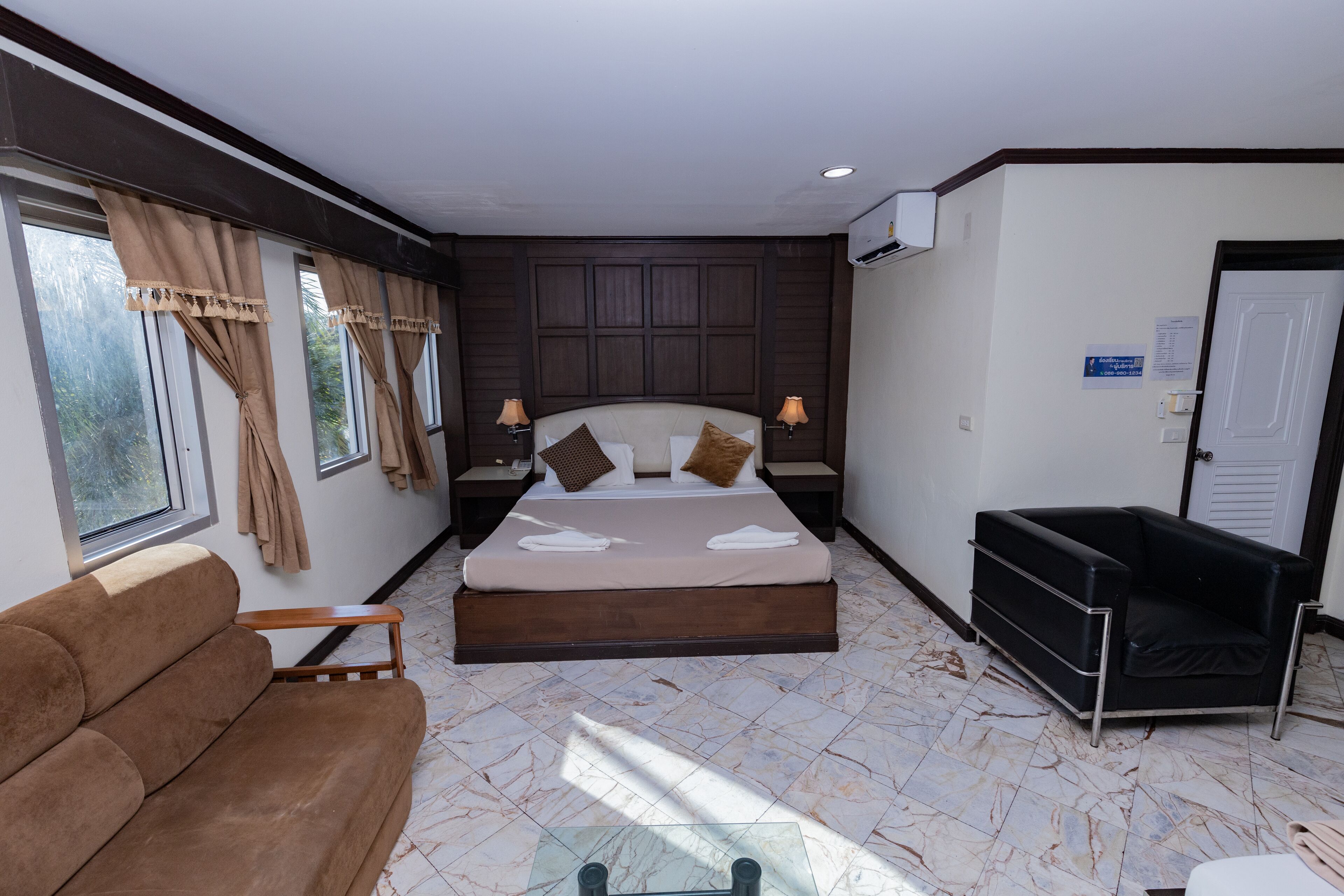 A hotel room with a bed, a brown sofa, a glass coffee table, and a black armchair.