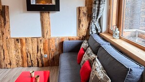 A cozy seating area with a built-in fireplace, wooden wall paneling, and a window with a view.