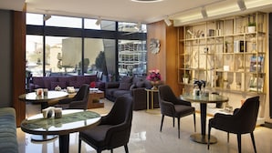 A modern lobby with a sofa, chairs, a coffee table, a bookshelf, and large windows offering a view of the city.