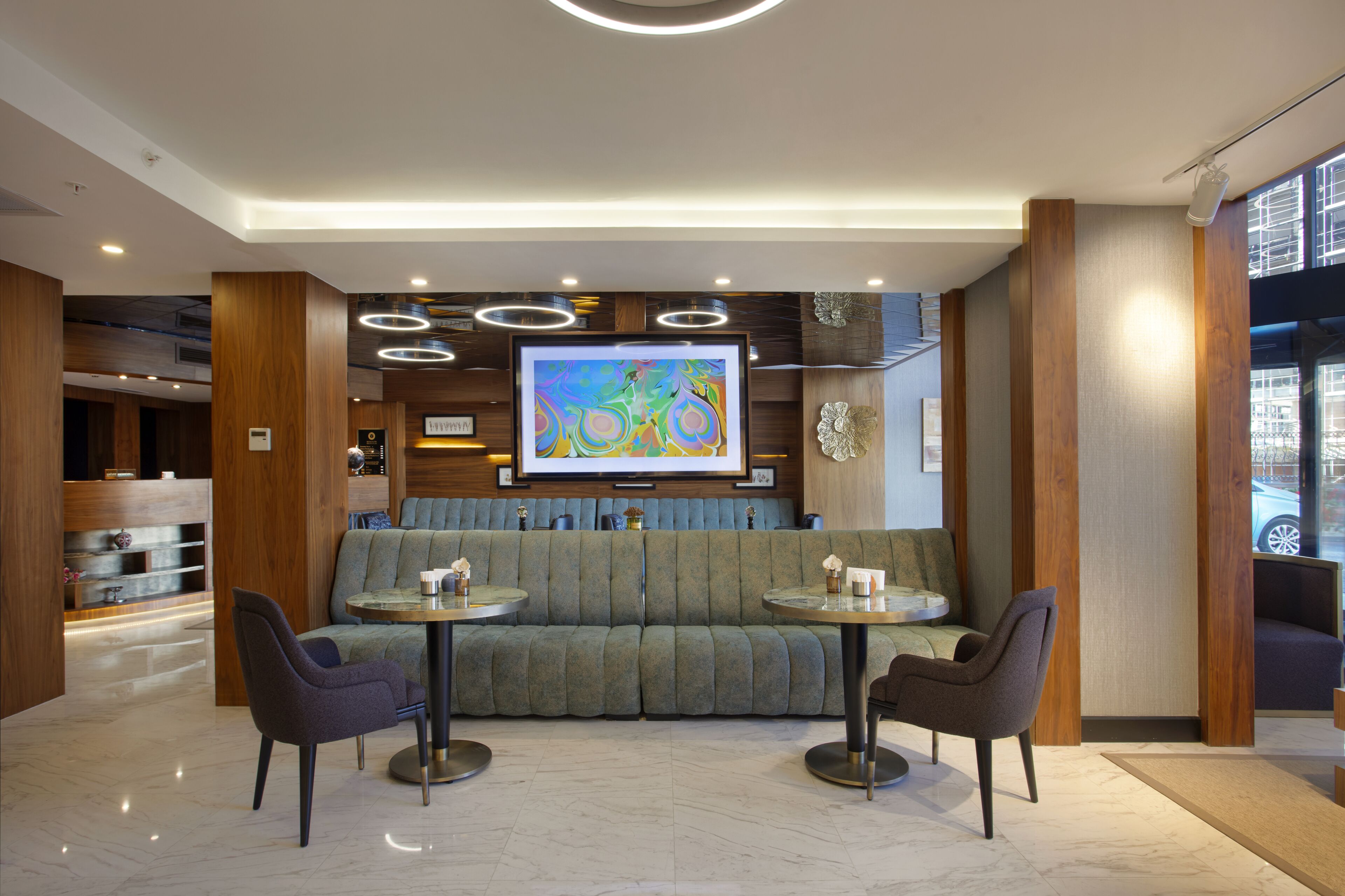 Un hall d’entrée moderne avec un canapé vert, deux tables rondes et un grand tableau abstrait accroché au mur.