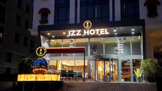 The exterior of the IZZ HOTEL with a prominent entrance, glass facade, and a well-lit sign.
