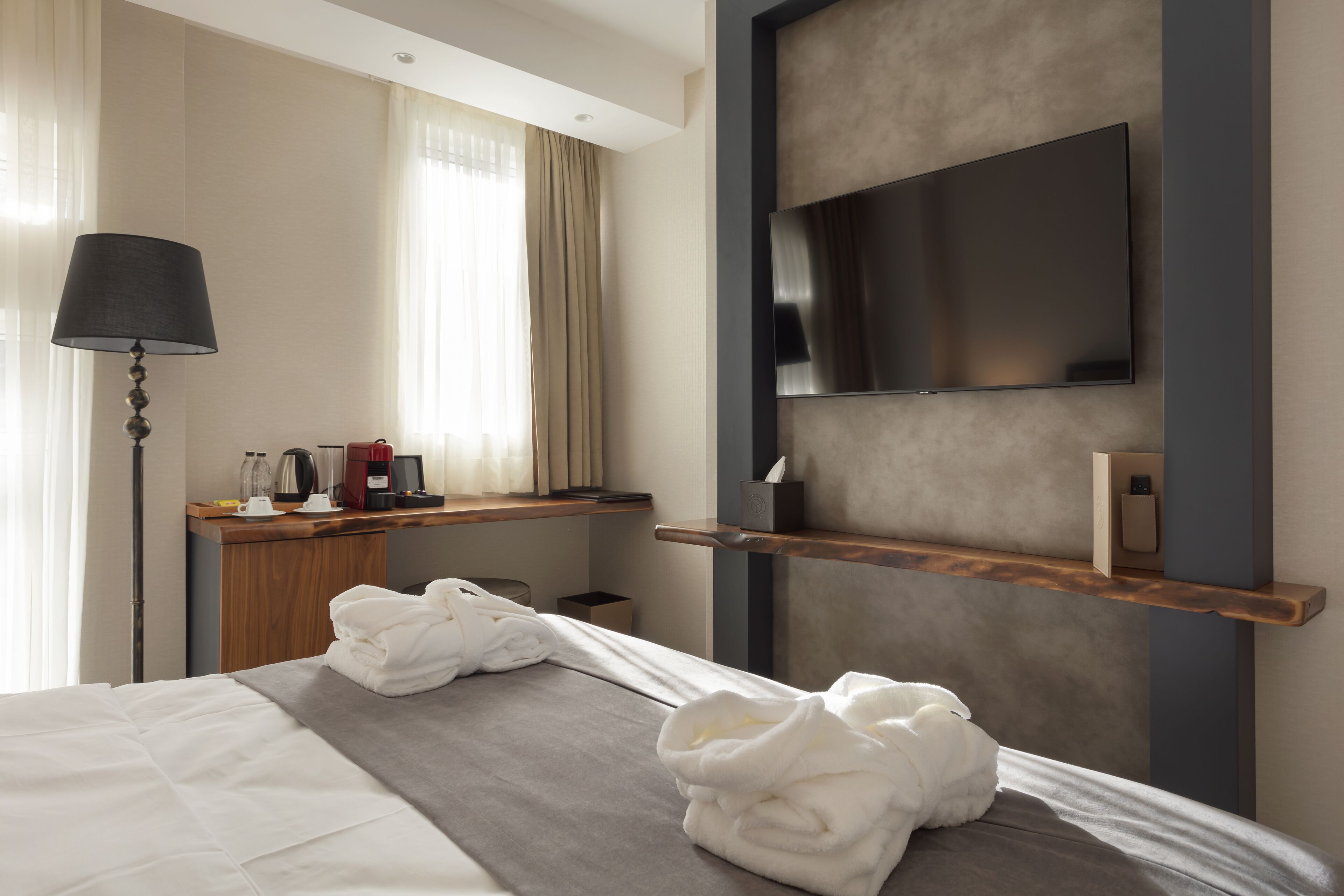 Een hotelkamer met een bed, een bureau met lamp, een aan de muur bevestigde televisie en een raam met gordijnen.