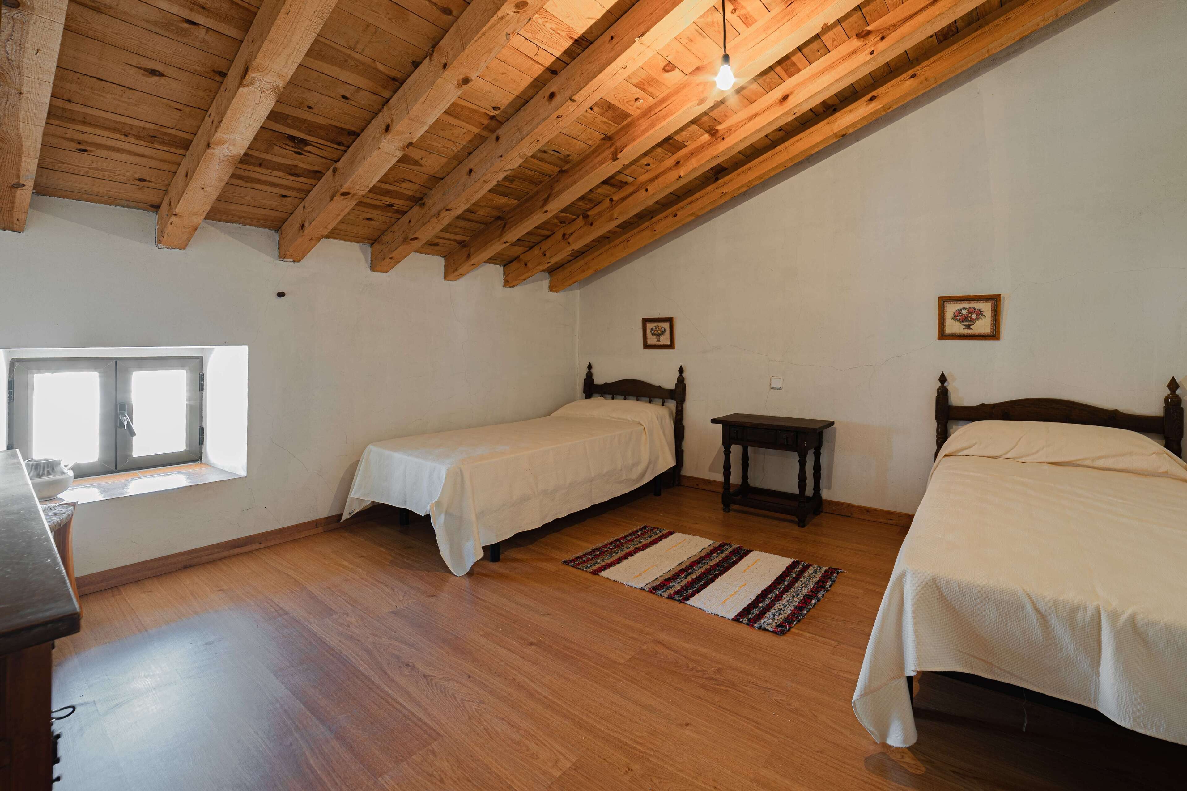 Un dormitorio con dos camas, suelo de madera, una ventana y techo de madera.