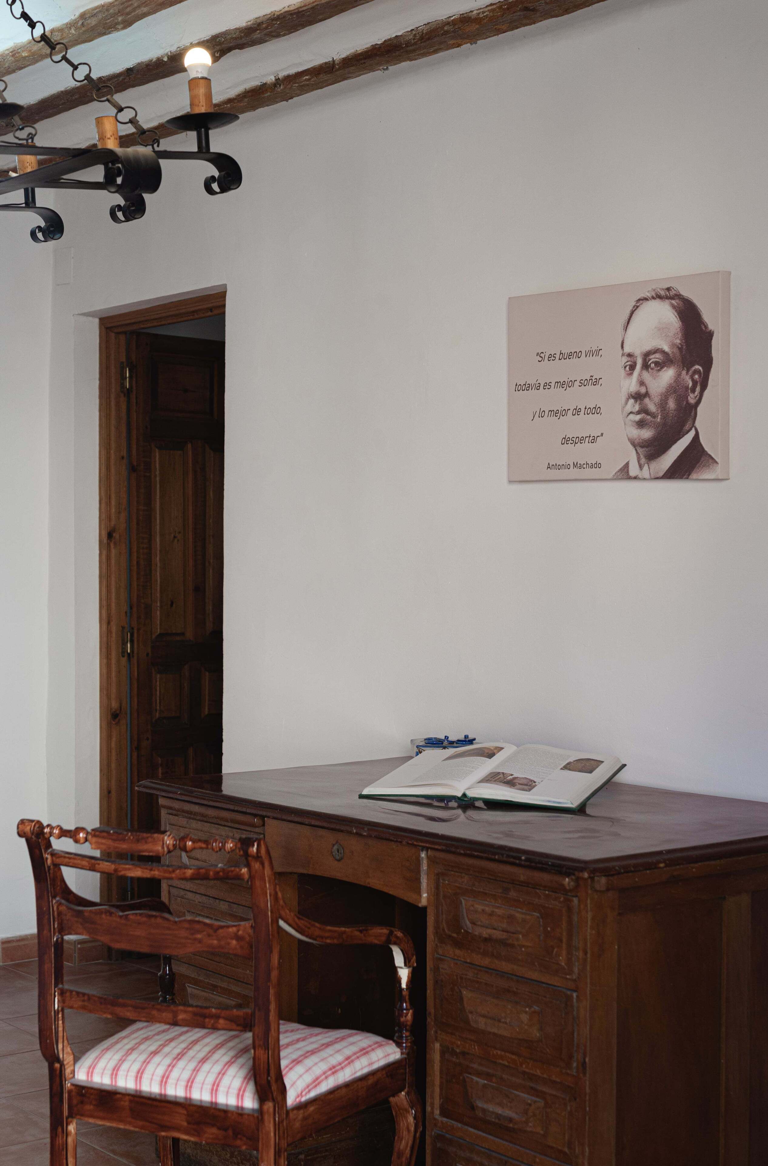 Una habitación con un escritorio de madera, una silla con cojín a rayas y un cartel colgado en la pared.