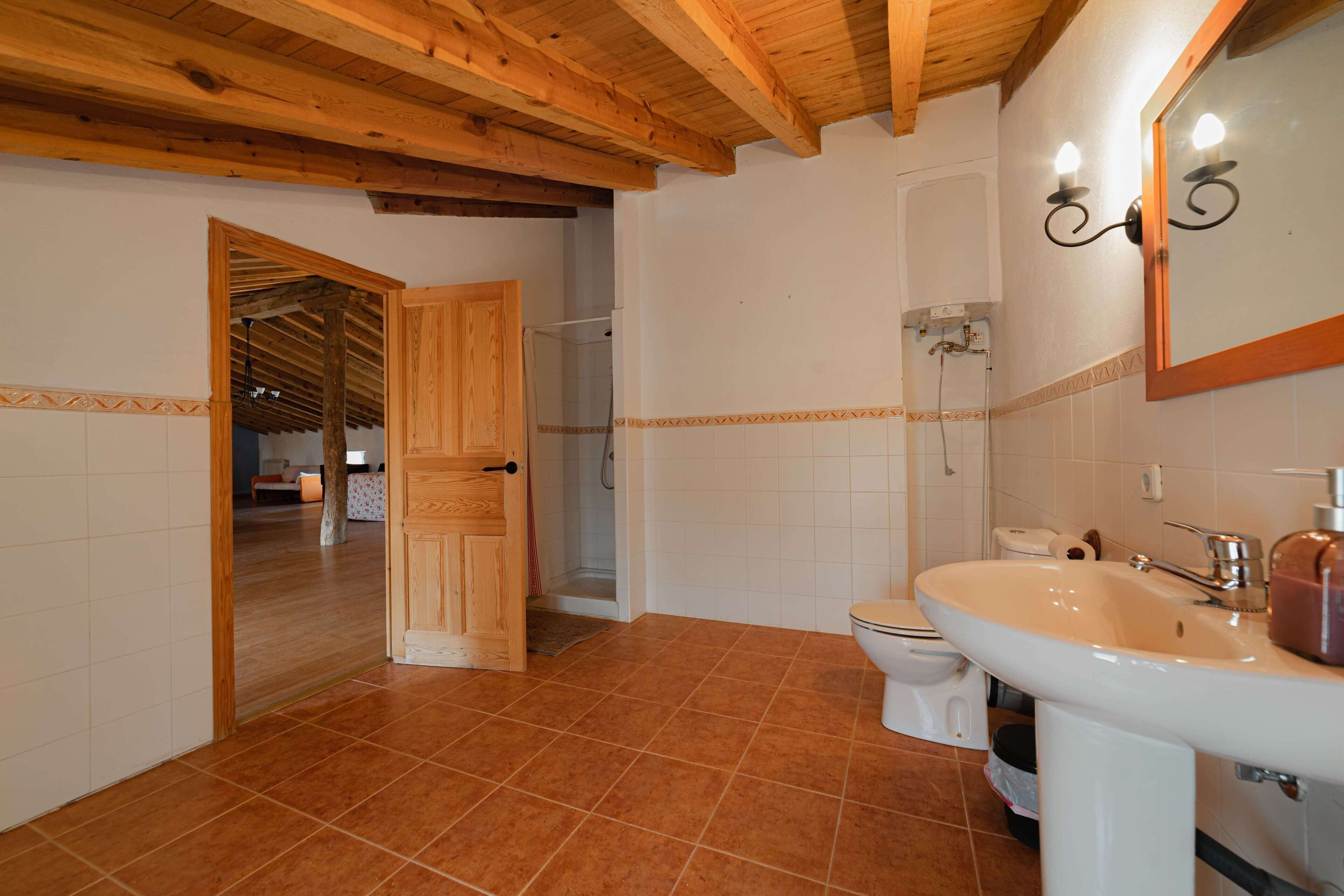 Un baño con techo de madera, azulejos blancos, un lavamanos, un inodoro y una zona de ducha.
