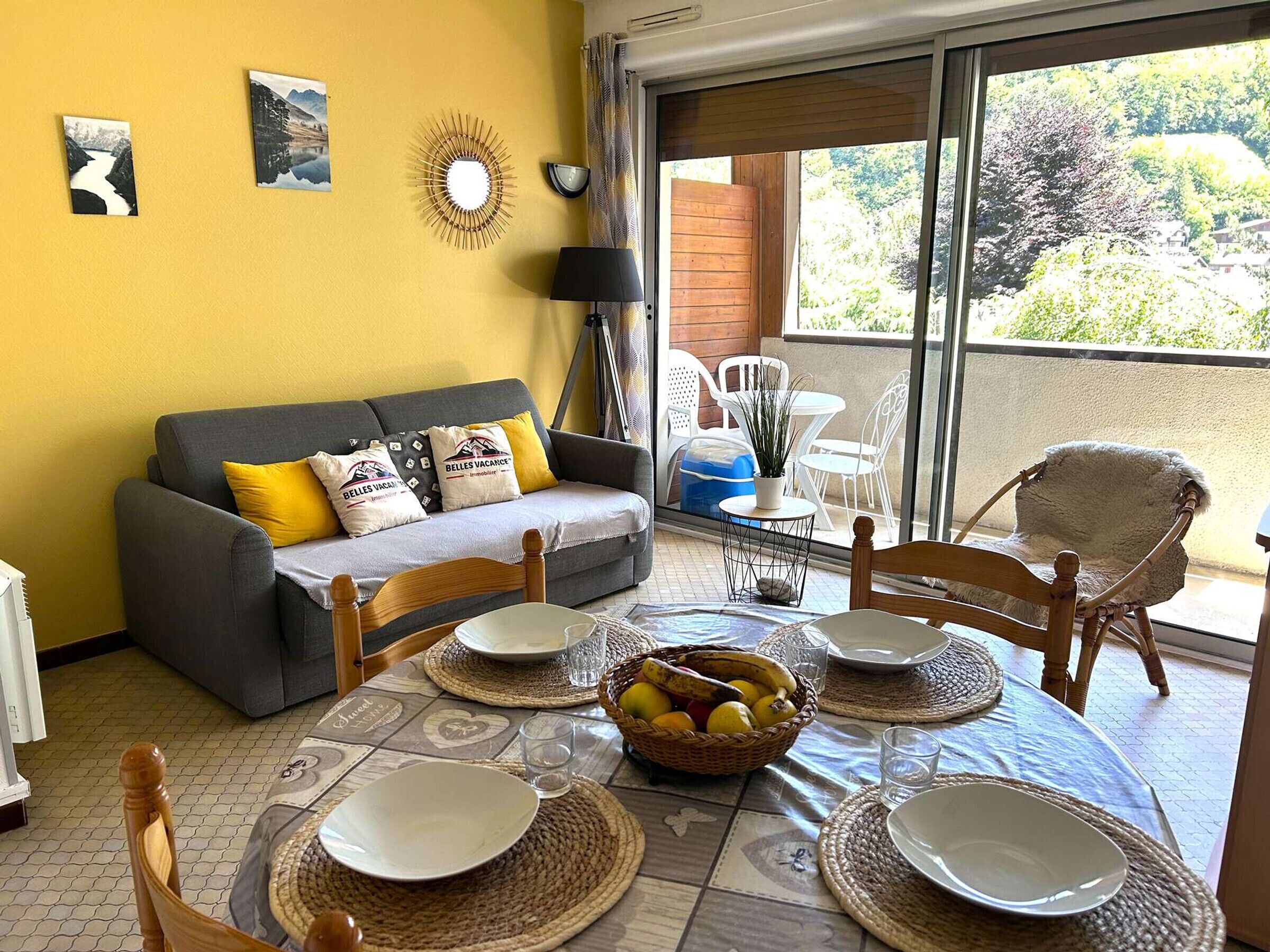 Un coin repas avec une table dressée pour quatre personnes, un canapé avec des coussins et une vue à travers une porte-fenêtre coulissante.
