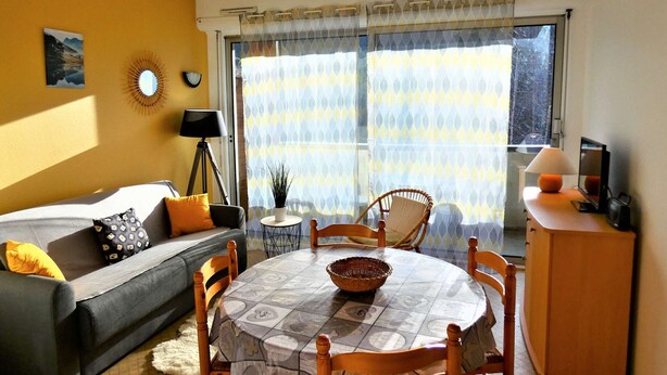 A living room with a sofa, a dining table with chairs, a lamp, and a television on a cabinet.