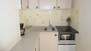 A compact kitchen with white cabinets, a built-in oven, and a coffee maker.
