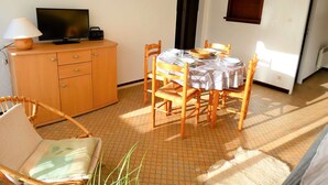 A dining area with a table set for two, a television on a wooden cabinet, and a clock on the wall.