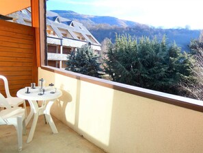 Un balcón con mesa y sillas, con vistas a un paisaje montañoso de árboles de coníferas y un edificio con techo inclinado.