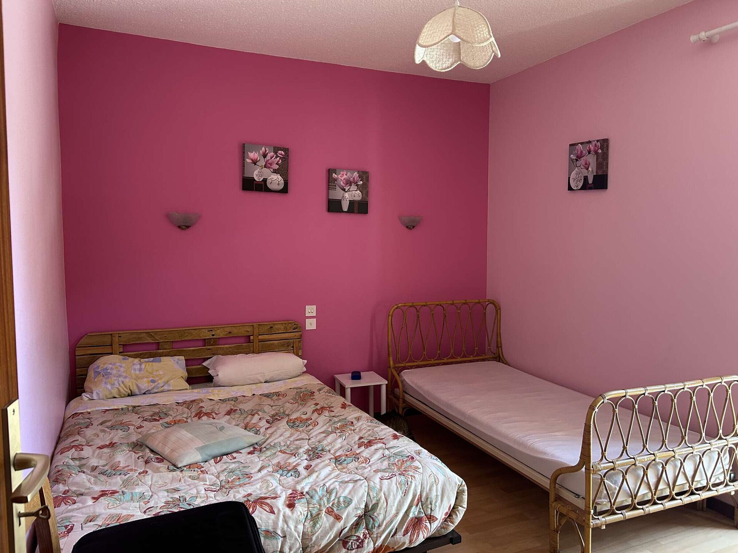 Een slaapkamer met een groot bed, een klein eenpersoonsbed, een nachtkastje en een wandlamp.