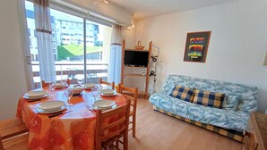 Un coin repas avec une table ronde dressée pour quatre personnes, un canapé bleu orné de coussins à motifs et un téléviseur fixé au mur.