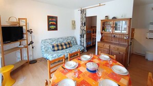Un salon chaleureux avec un canapé, une table à manger dressée pour quatre personnes, un téléviseur posé sur une étagère et un meuble avec des portes en verre.