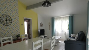 A dining area with a white table and chairs, a TV, and a sofa in a room with yellow walls and a patterned wallpaper. - Pleasant bright house with terrace and garden (Plaisance-du-Touch)