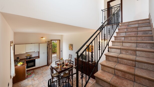 A spacious kitchen with modern appliances, a dining area with a table set for four, and a staircase with a metal railing leading to an upper floor.