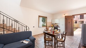 A living room with a blue sofa, a dining table with chairs, a kitchen area, and a staircase.