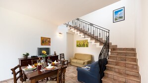 A dining area with a wooden table set for four, a sofa, and a staircase with a black railing.