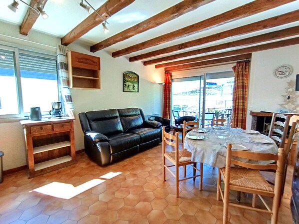 Una sala de estar acogedora con un sofá de cuero negro, una mesa de comedor de madera para cuatro personas y un suelo de baldosas hexagonales.