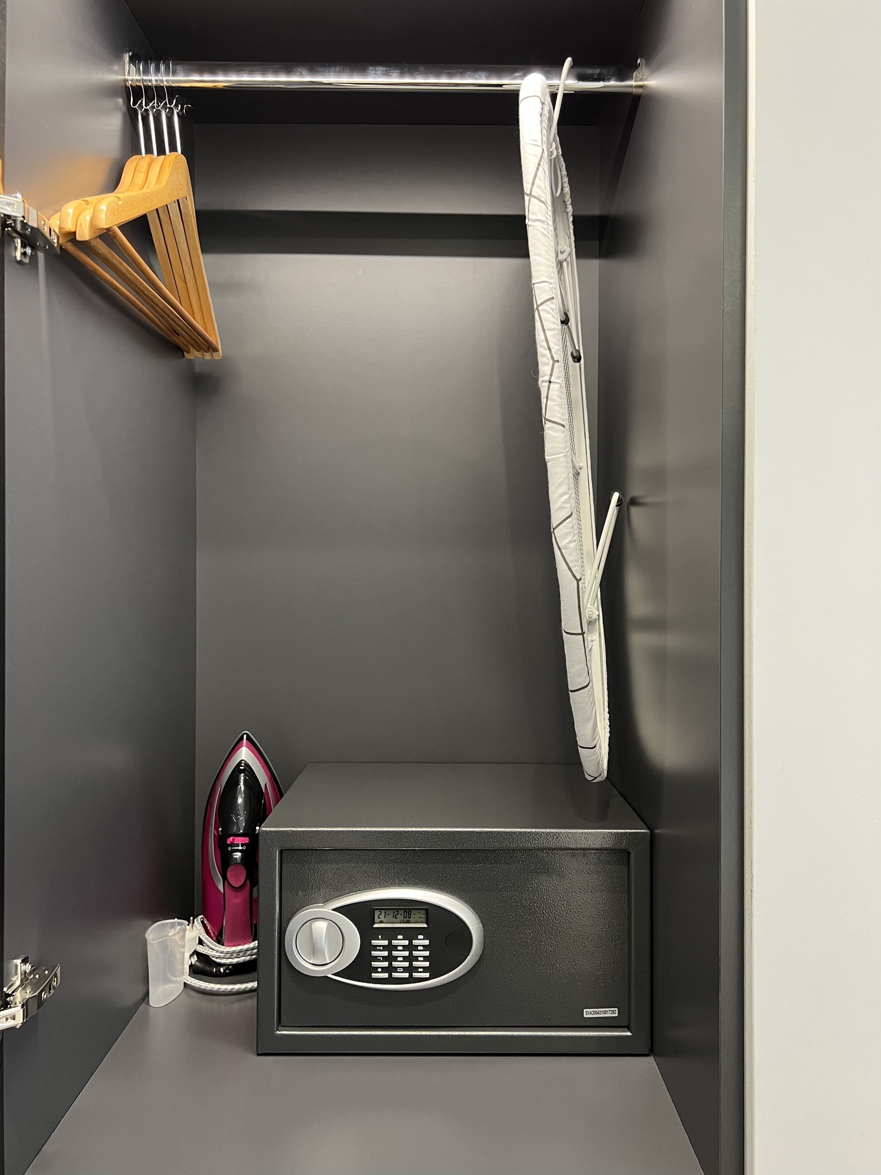 A compact, modern room with a built-in microwave, a small ironing board, and a hanging garment.