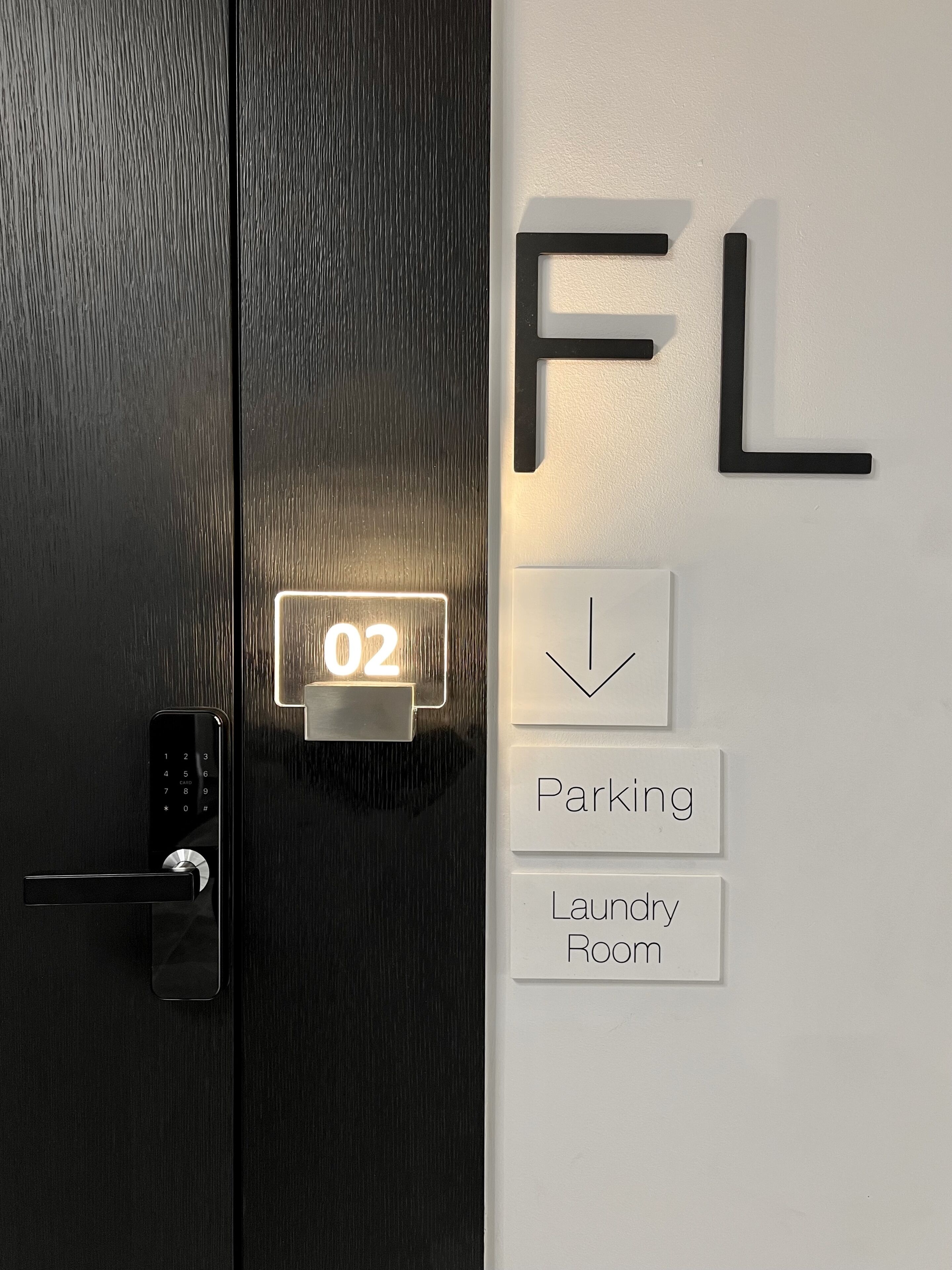 A door with a digital lock and a keypad, a wall-mounted sign with the letters "FL", and a sign indicating "Parking" and "Laundry Room" below.