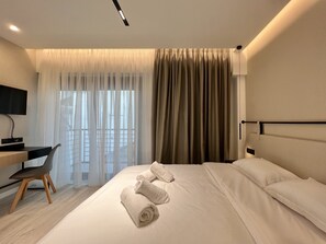 Quarto de hotel com cama, escrivaninha, cadeira e televisão fixada na parede.