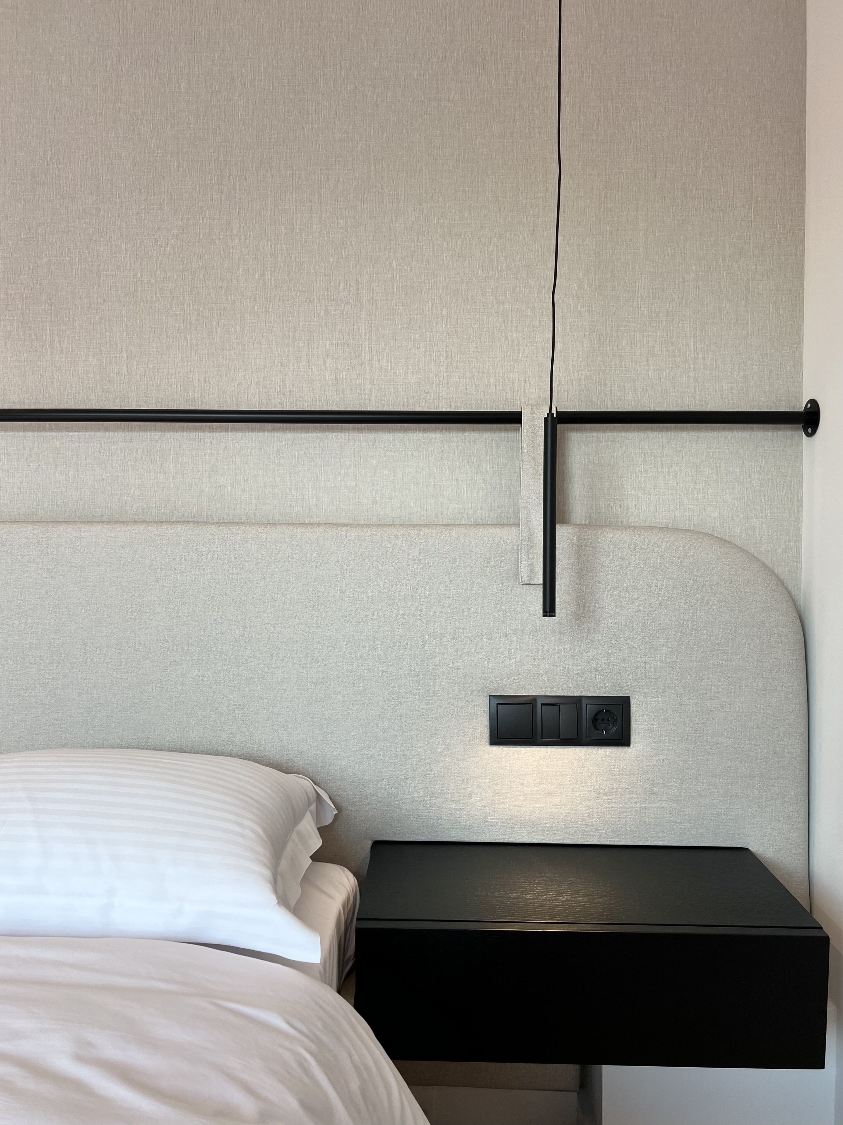 A modern hotel room with a bed, a bedside table, and a headboard with a control panel.