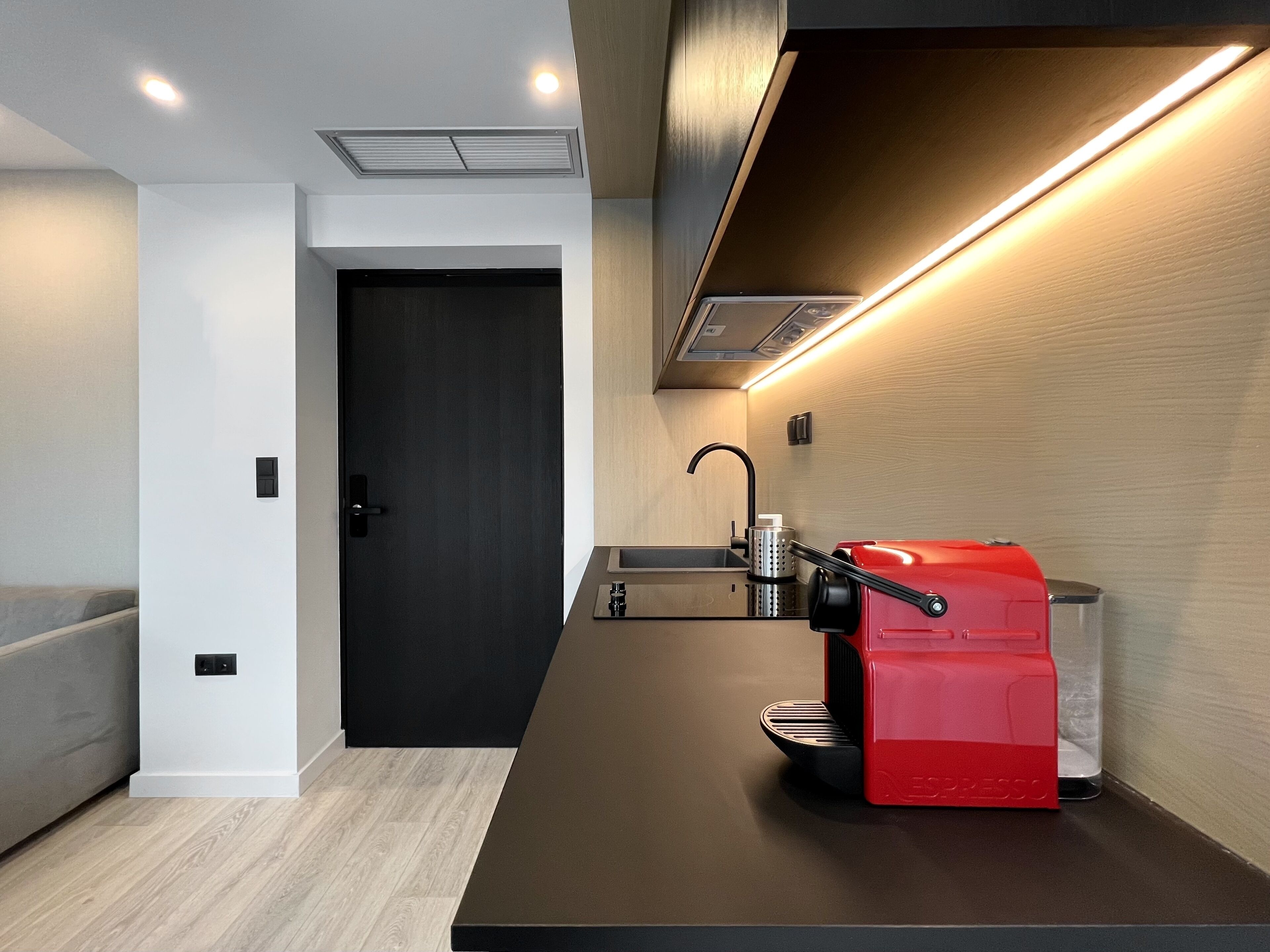 Una cocina moderna con cafetera espresso integrada, una puerta negra y un revestimiento de pared en madera clara.
