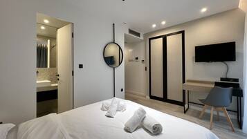 A modern hotel room with a bed, a desk, a TV, and a bathroom visible through an open door.