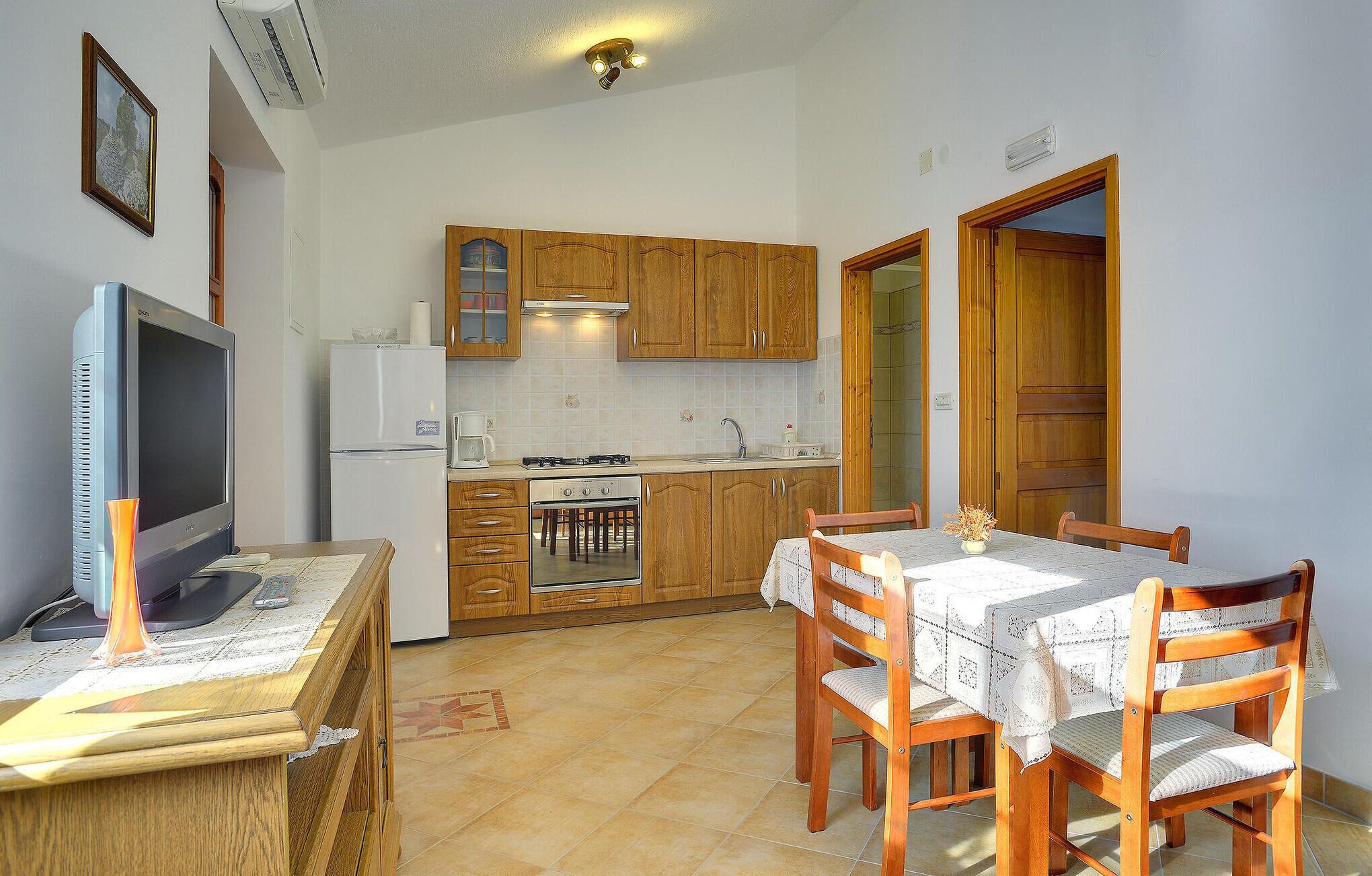 A compact kitchen with wooden cabinets, a refrigerator, a stove, and a dining table with chairs.