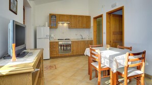 A compact kitchen with wooden cabinets, a refrigerator, a stove, and a dining table with chairs. - 1 bedroom awesome apartment in Rakalj (Rakalj)