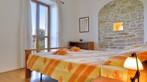 A bedroom with a wooden bed, a stone wall, a window with curtains, and a bedside lamp. - 1 bedroom awesome apartment in Rakalj (Rakalj)