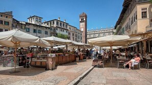 A bustling outdoor market with vendors and customers, stone pavement, and historic buildings in the background. - Il Cardo - Royal Solution (Verona)