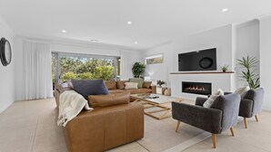 A modern living room with a brown leather sofa, grey armchairs, a coffee table, and a fireplace. - Que Syrah - 5 bedroom house with 4 bathrooms (POKOLBIN)