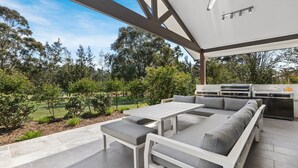 An outdoor patio with a built-in grill and seating area, surrounded by trees and a lawn. - Que Syrah - 5 bedroom house with 4 bathrooms (POKOLBIN)