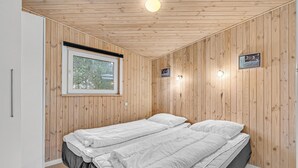 A room with wooden walls, a bed with white bedding, a window with a view of trees, and a wall-mounted light fixture. - Cozy home in Roslev with WiFi (Roslev)