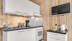 A modern kitchen with white cabinets, a black countertop, a built-in oven, a coffee maker, and a TV mounted on the wall. - Cozy home in Roslev with WiFi (Roslev)