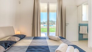 Et hotelværelse med seng, gardiner, udsigt til en pool og et badeværelse med håndklædestige.