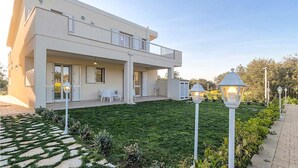 Et moderne hus i to etager med en overdækket terrasse, udendørs møbler og en velplejet græsplæne.