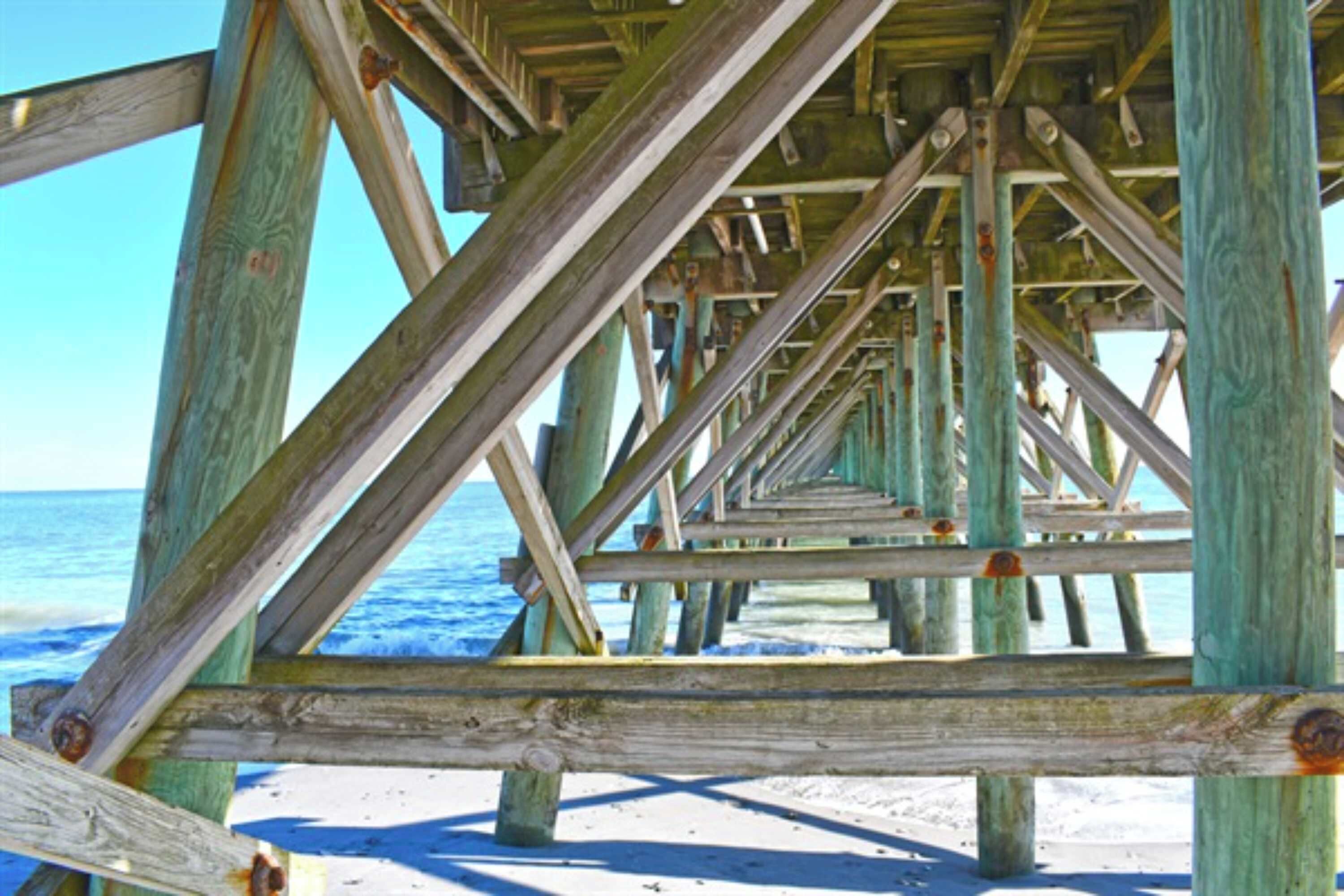 A wooden pier structure with a clear view of the ocean and beach.
