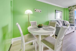 Un espace repas avec une table ronde, des chaises blanches et un mur vert.