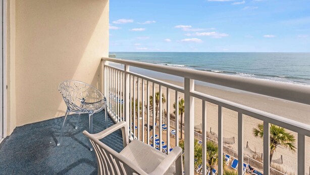 A balcony with a clear view of the beach, a chair, and a table. - Direct Oceanfront View Suite,Pools at Sandy Beach! (Myrtle Beach)