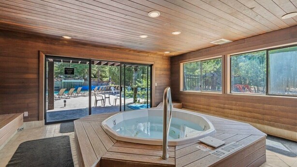 Un área de piscina interior moderna con un jacuzzi, suelo de madera y grandes ventanales con vistas al exterior.